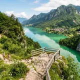 Sentiero panoramico sul lago di Val Cellina a Barcis, con escursionisti e montagne verdi.