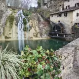 Antico mulino ad acqua accanto a cascate e grotte in Veneto, con un laghetto verde e vegetazione rigogliosa.