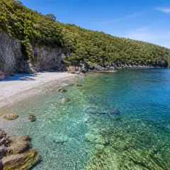 Spiaggia Maratea: scogliera verdeggiante, ciottoli bianchi e acque cristalline che invitano a un tuffo.
