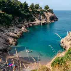 Una piccola spiaggia a Sorrento, con acque cristalline e rocce scoscese. Alcune persone si rinfrescano in mare.