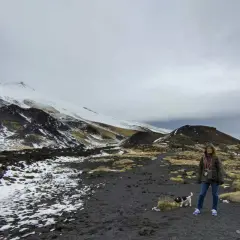 Una donna e il suo cane esplorano il paesaggio lunare dell'Etna in Sicilia, con neve e rocce vulcaniche.