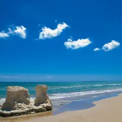 Spiagge attrezzate Sicilia: rocce scolpite dal mare e sabbia dorata sotto un cielo azzurro con nuvole bianche.