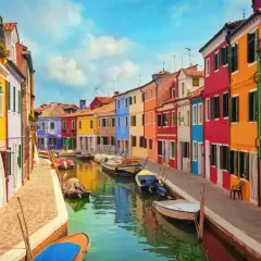 Colorate case affacciate su un canale a Burano, vicino a Murano. Barche ormeggiate riflettono i colori vivaci.