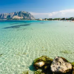 Acque cristalline e un promontorio maestoso fanno da sfondo a una giornata di sole al mare a Palermo.