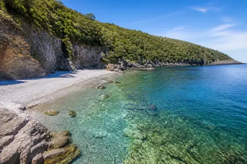 Spiaggia Maratea: scogliera verdeggiante, ciottoli bianchi e acque cristalline che invitano a un tuffo.