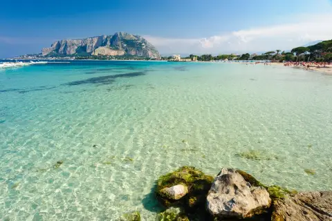 Acque cristalline e un promontorio maestoso fanno da sfondo a una giornata di sole al mare a Palermo.