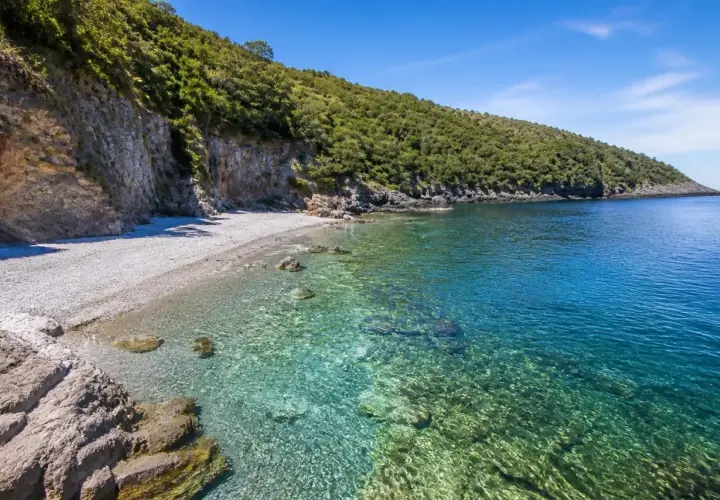 Spiaggia Maratea: scogliera verdeggiante, ciottoli bianchi e acque cristalline che invitano a un tuffo.