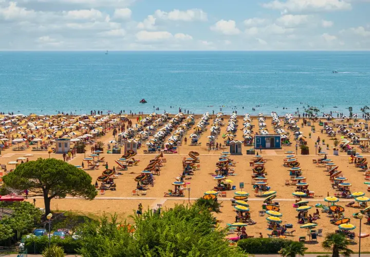 Una spiaggia affollata vicino a Venezia, con file ordinate di ombrelloni gialli e bianchi e persone che si godono il sole e il mare azzurro.