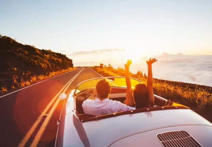 Coppia in auto decappottabile al tramonto, con le braccia alzate, godendosi un itinerario Croazia da sogno.