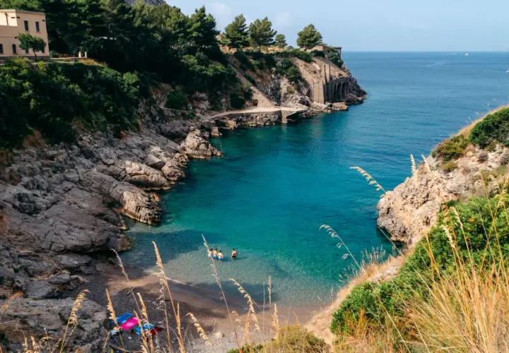 Una piccola spiaggia a Sorrento, con acque cristalline e rocce scoscese. Alcune persone si rinfrescano in mare.
