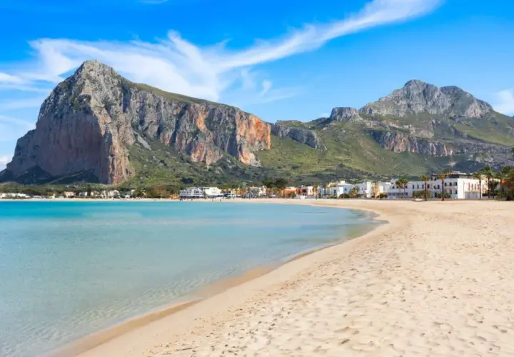 Spiaggia di San Vito Lo Capo, Sicilia, con acque turchesi e montagne imponenti sullo sfondo. Un paradiso per chi ama il mare.