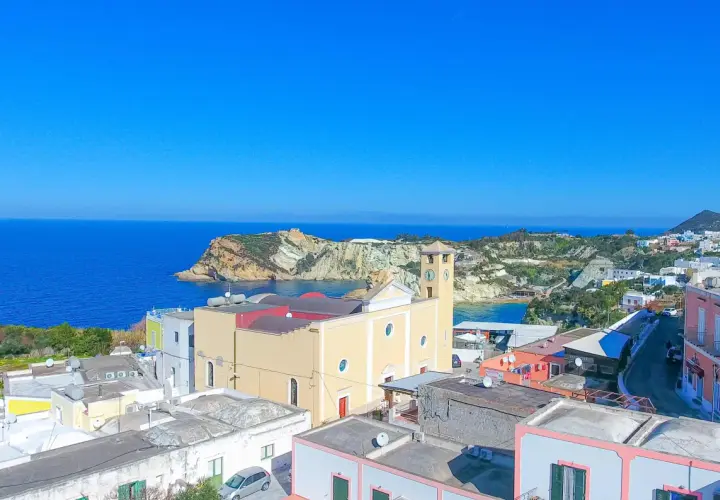 Vista panoramica dell'isola di Ponza con case colorate, una chiesa con campanile e il mare blu intenso.