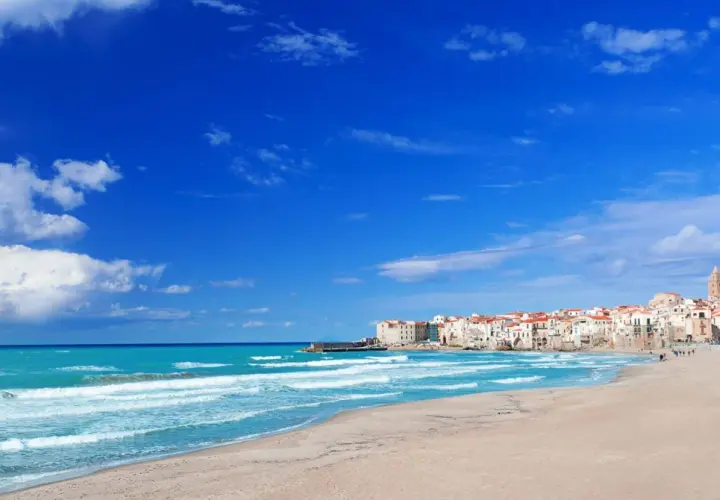 Spiaggia di Palermo con mare turchese e case bianche con tetti rossi.