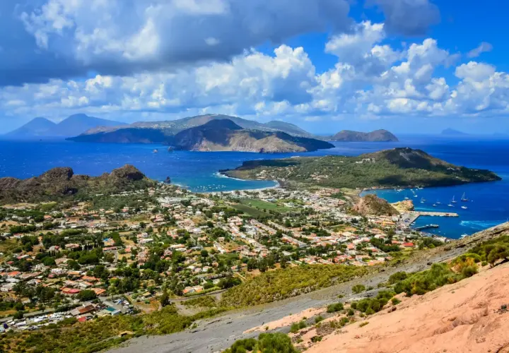 Panoramica mozzafiato delle isole Eolie, tra le isole più belle della Sicilia, con case bianche, vegetazione lussureggiante e mare blu intenso.