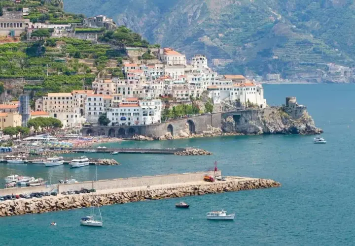 Amalfi: cosa vedere in un giorno. La pittoresca cittadina si affaccia sul mare blu, con case bianche aggrappate alla collina e un porto pieno di barche.