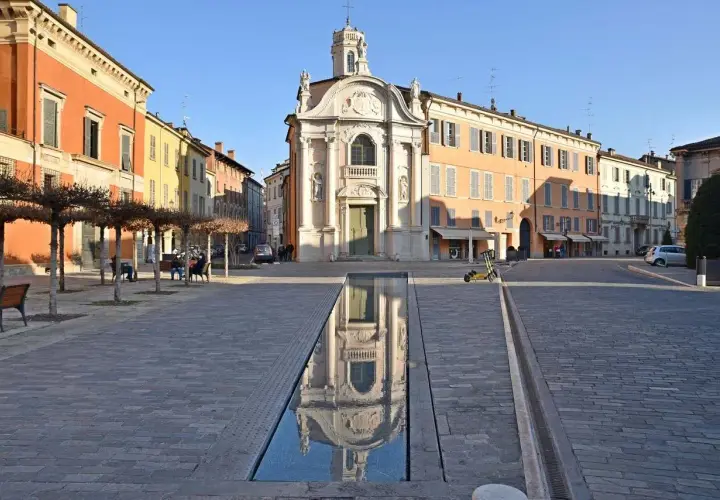 Piazza con chiesa barocca e specchio d'acqua, ideale per scoprire cosa vedere a Reggio Emilia in un giorno.