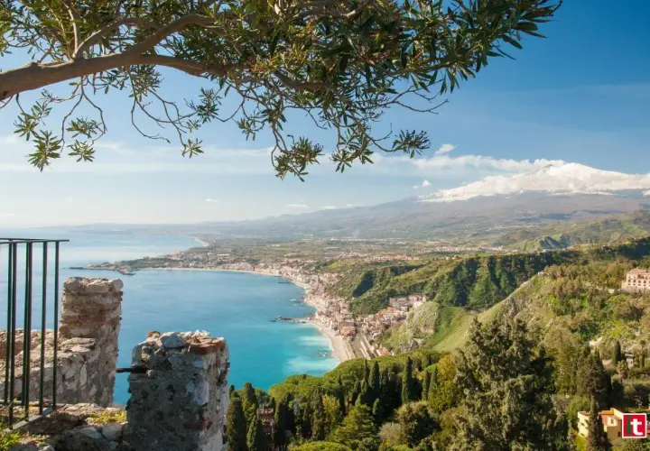 Vista panoramica di Naxos, Sicilia, con il mare azzurro, la costa e l'Etna innevato sullo sfondo, incorniciata da un ramo d'ulivo.