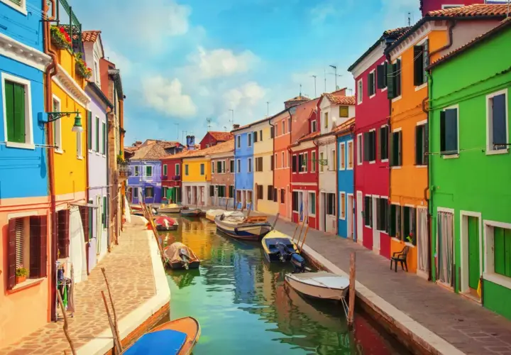 Colorate case affacciate su un canale a Burano, vicino a Murano. Barche ormeggiate riflettono i colori vivaci.