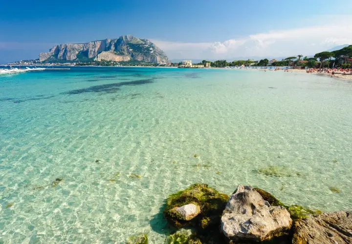 Acque cristalline e un promontorio maestoso fanno da sfondo a una giornata di sole al mare a Palermo.