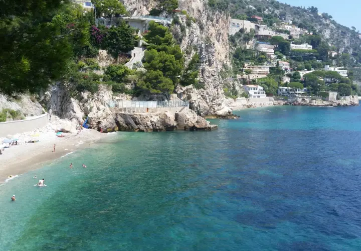 Spiaggia di Eze-sur-Mer con ville aggrappate alla scogliera e acque turchesi cristalline.