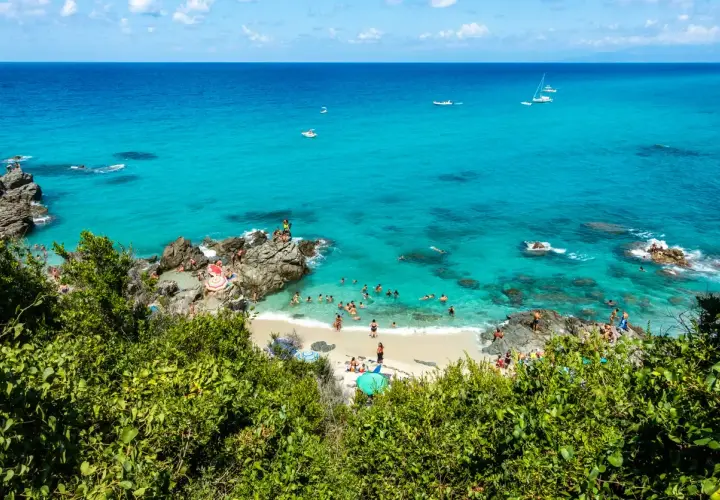 Spiaggia con acque cristalline e gente che nuota e prende il sole. Un luogo ideale per il tuo prossimo viaggio in Calabria mare dove andare.