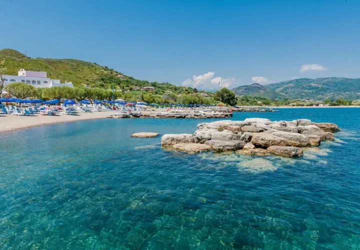 Spiaggia attrezzata con ombrelloni e lettini, mare cristallino e rocce affioranti. Un angolo di paradiso nel Cilento, mare da sogno.