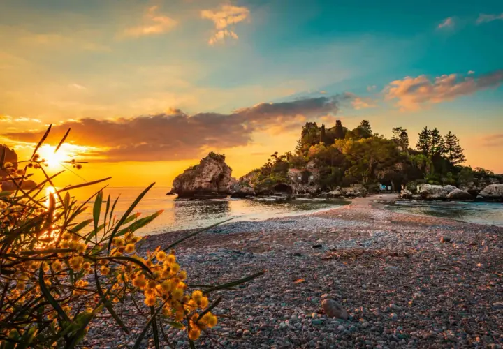 Tramonto dorato sulle spiagge di Giardini Naxos Taormina, con rocce e vegetazione lussureggiante.