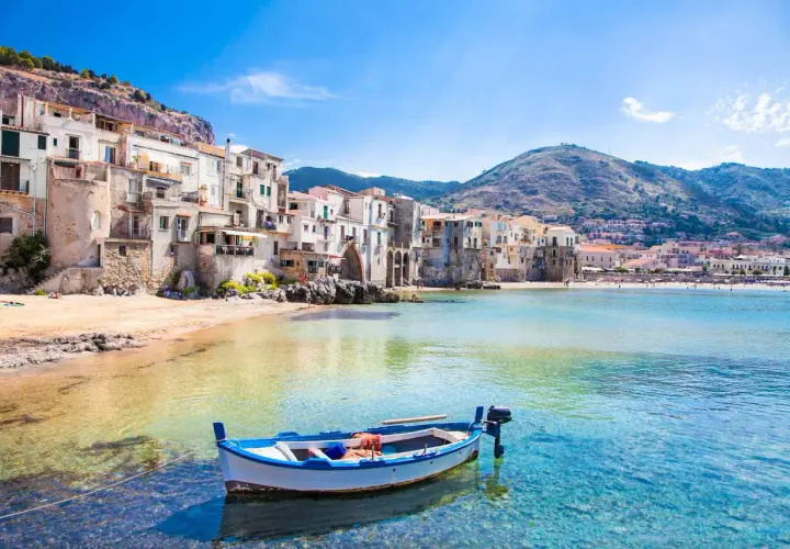 Barca a remi in acque cristalline davanti a Cefalù, con le sue case colorate e le spiagge più belle che invitano al relax.