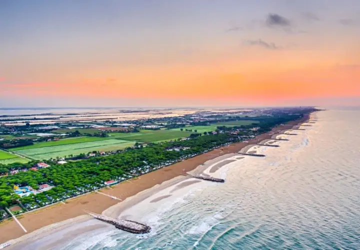 Alba sul mare veneto, con la spiaggia dorata, pineta rigogliosa e lagune all'orizzonte.