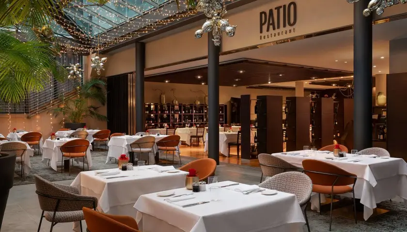Atmosfera elegante al Patio Restaurant, un'ottima opzione per chi cerca dove mangiare a Bolzano. Tavoli apparecchiati sotto luci soffuse e piante rigogliose.