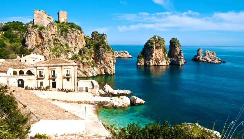 Torri e case antiche su scogliere rocciose, con faraglioni nel mare blu. Un paesaggio che evoca la storia dei bizantini in Sicilia.
