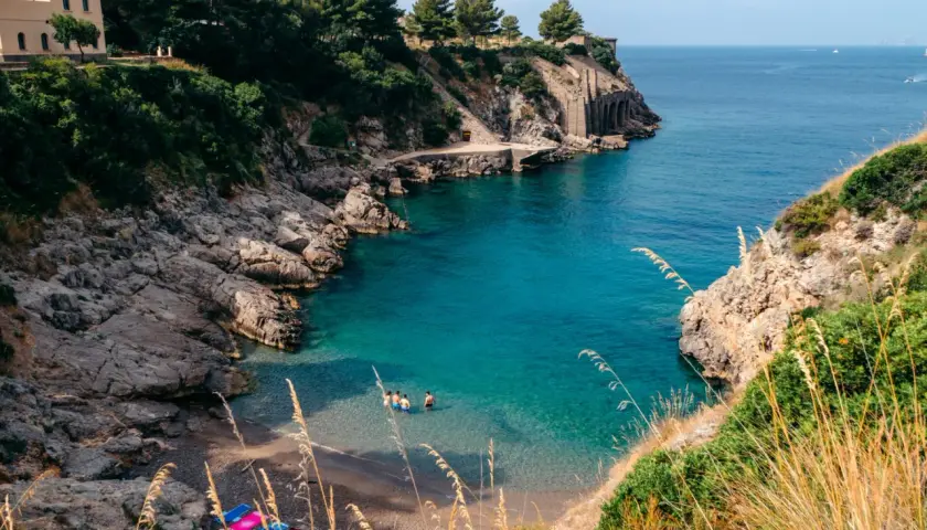 Una piccola spiaggia a Sorrento, con acque cristalline e rocce scoscese. Alcune persone si rinfrescano in mare.