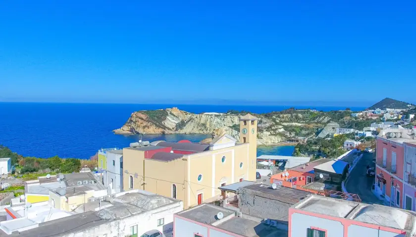 Vista panoramica dell'isola di Ponza con case colorate, una chiesa con campanile e il mare blu intenso.