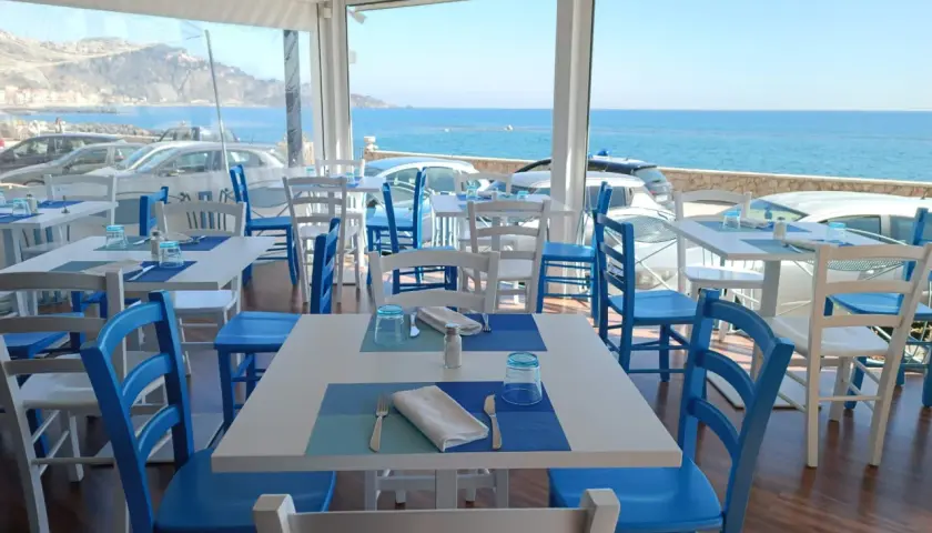 Tavoli apparecchiati con vista mare, perfetti per un apericena a Giardini Naxos. Sedie bianche e blu, un'atmosfera rilassante.