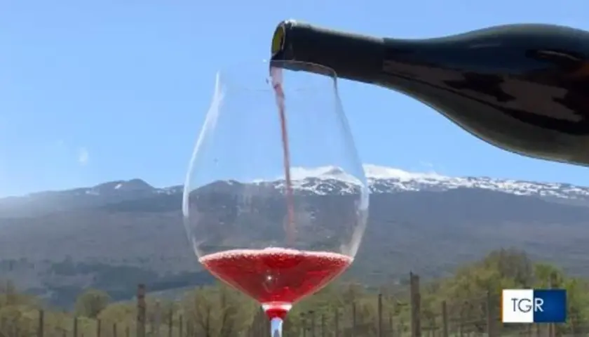 Versando vino rosso in un calice, con l'Etna innevato sullo sfondo. Un sorso di etna wine, un'esperienza unica.