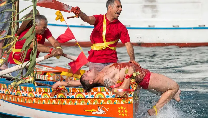 Uomo in barca siciliana, coperto di rosso, durante le feste. Un rematore con remo insanguinato.