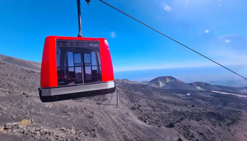 Cabina rossa della funivia in viaggio verso l'altezza Etna Rifugio Sapienza, su un paesaggio lunare di rocce laviche.