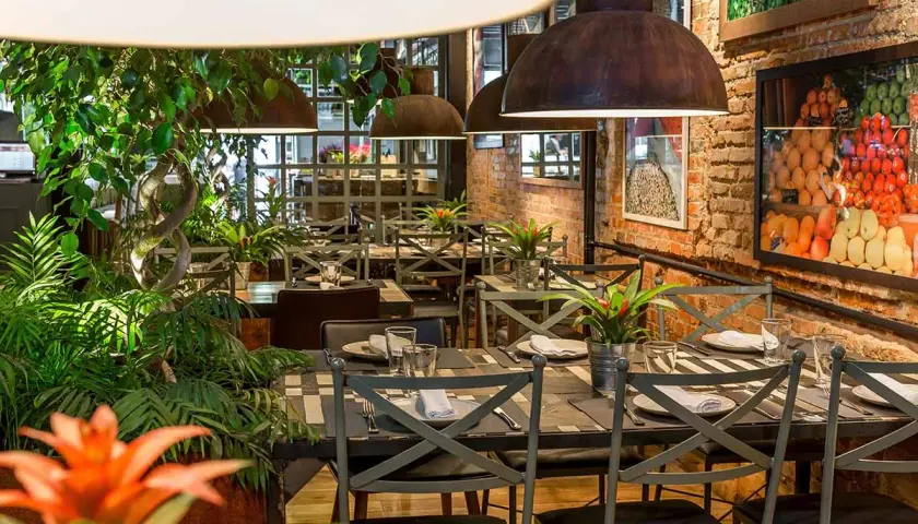 Tavoli apparecchiati in un ristorante con piante rigogliose e foto di frutta. Un'ottima opzione per sapere dove mangiare a Madrid.