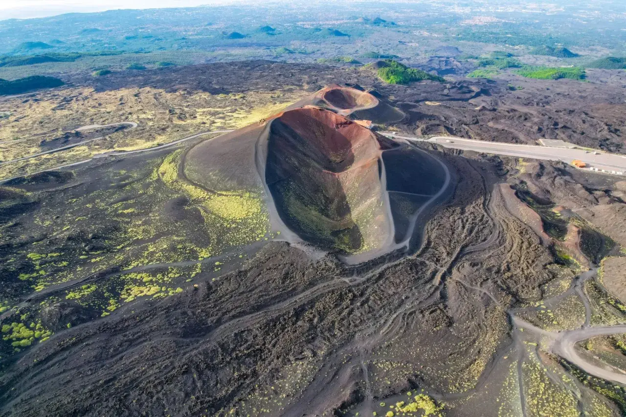 Vista aerea dei crateri spenti del vulcano Etna, con sentieri che si snodano tra la lava nera e la vegetazione gialla. Un'emozionante visita al Monte Etna.