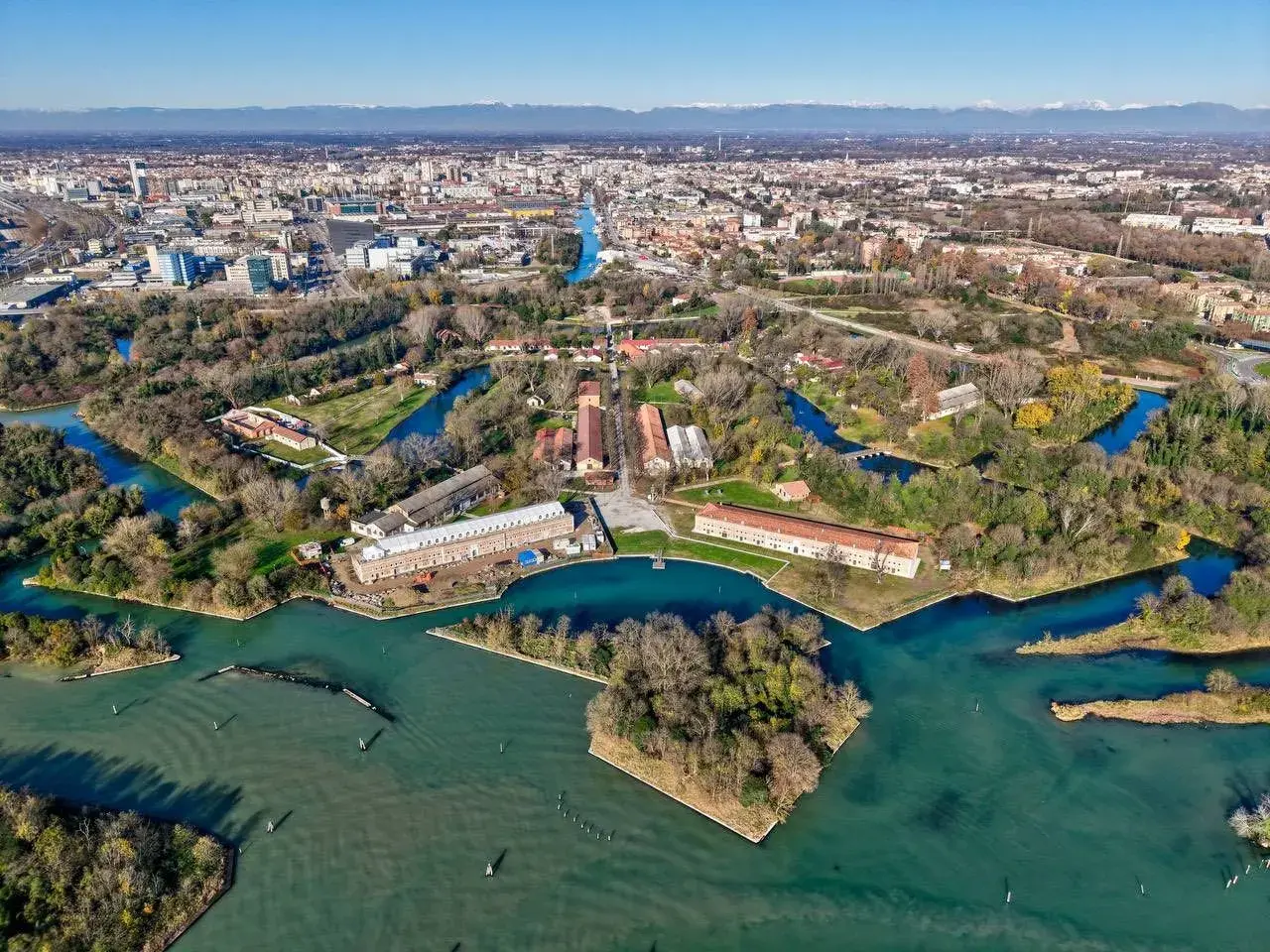Marghera: cosa vedere? Un'area verde con canali, edifici storici e la città sullo sfondo.