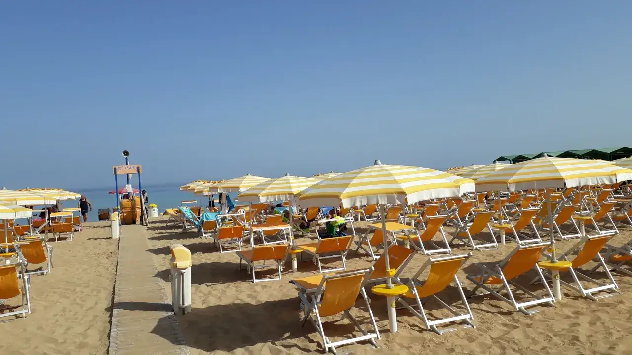 File di lettini e ombrelloni a righe gialle e bianche su sabbia dorata, tipiche delle spiagge attrezzate in Sicilia.