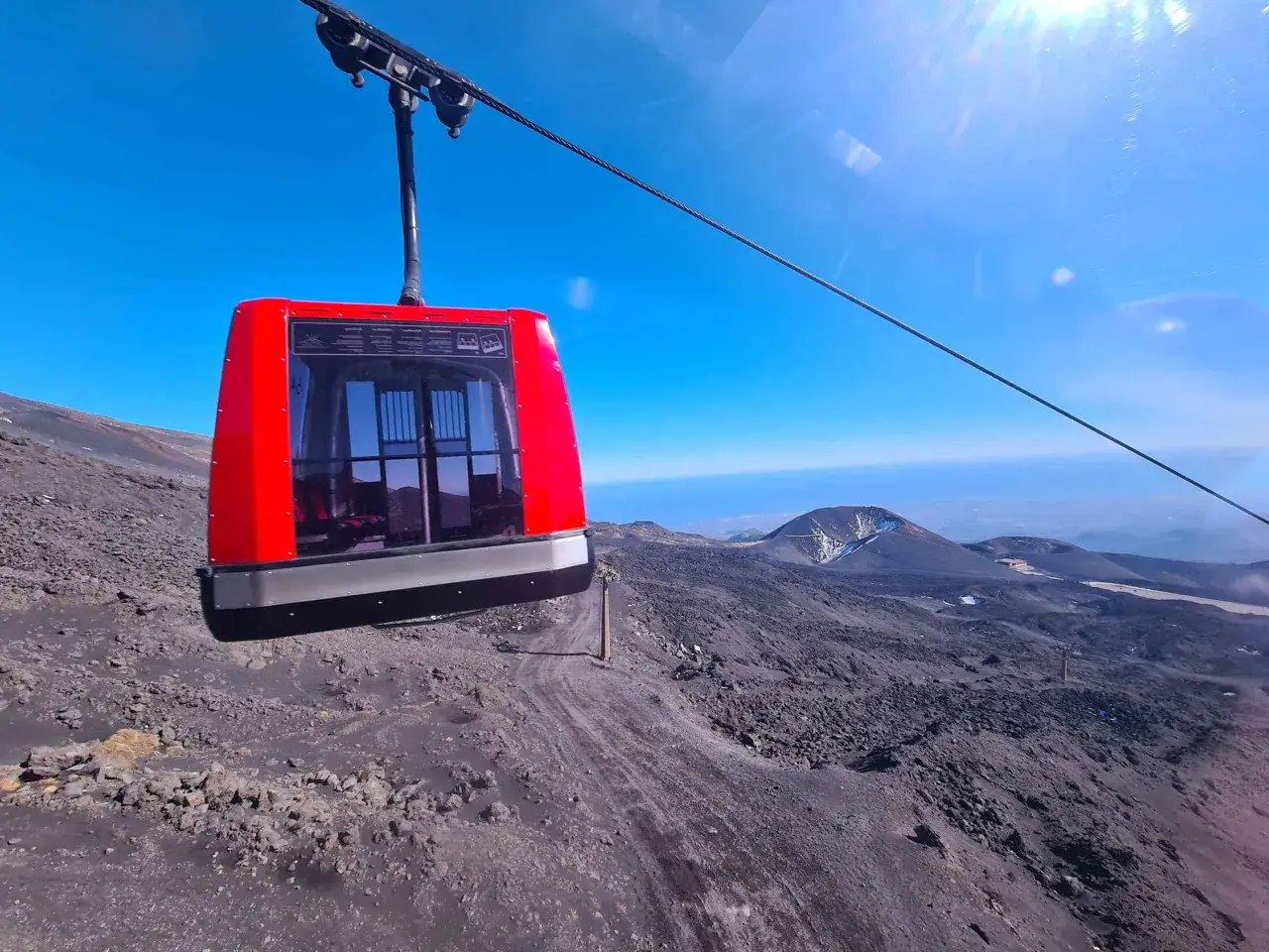 Cabina rossa della funivia sale verso la cima del vulcano, offrendo una vista mozzafiato del paesaggio lunare. Un'avventura indimenticabile per chi decide di visit mount Etna.