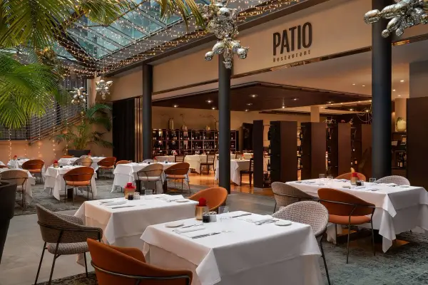 Atmosfera elegante al Patio Restaurant, un'ottima opzione per chi cerca dove mangiare a Bolzano. Tavoli apparecchiati sotto luci soffuse e piante rigogliose.