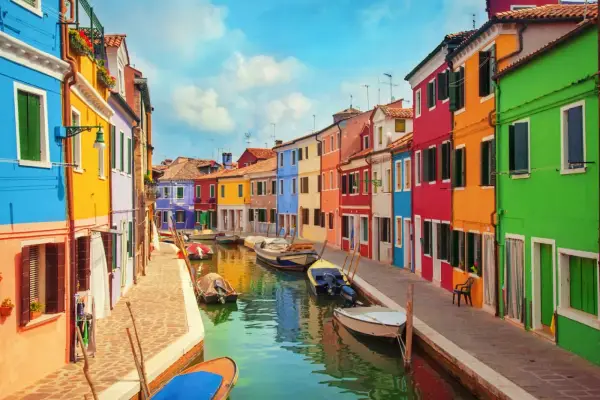 Colorate case affacciate su un canale a Burano, vicino a Murano. Barche ormeggiate riflettono i colori vivaci.